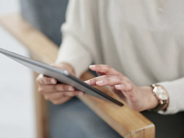 Eine Person sitzt auf einem Stuhl und hält ein Tablet in der Hand, während sie mit den Fingern auf den Bildschirm tippt.