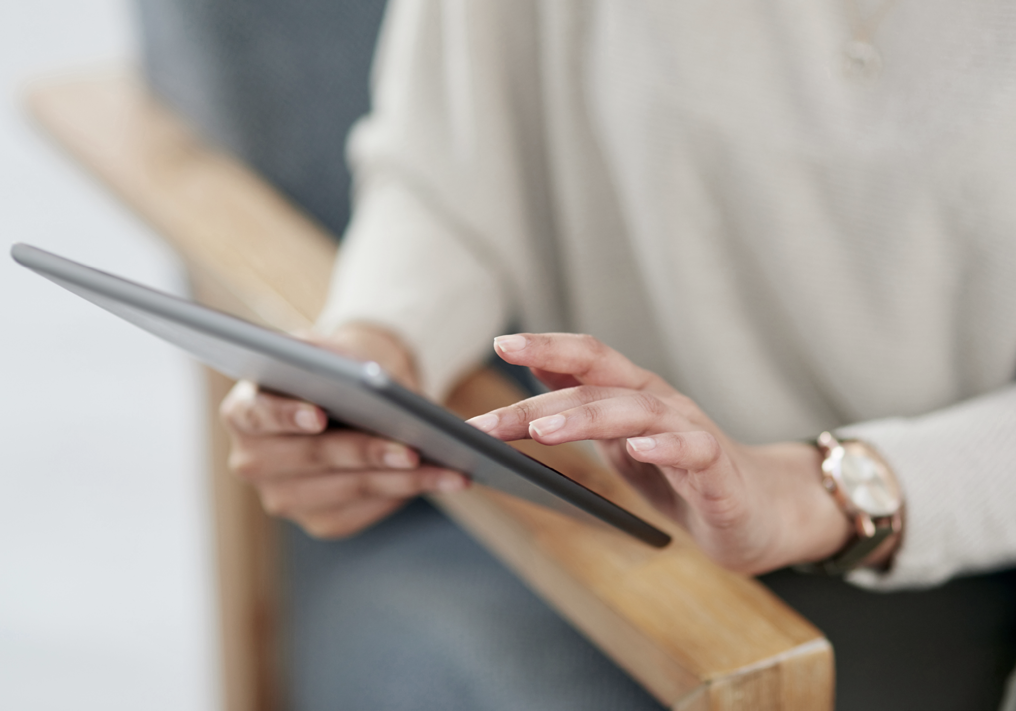 Eine Person sitzt auf einem Stuhl und hält ein Tablet in der Hand, während sie mit den Fingern auf den Bildschirm tippt.
