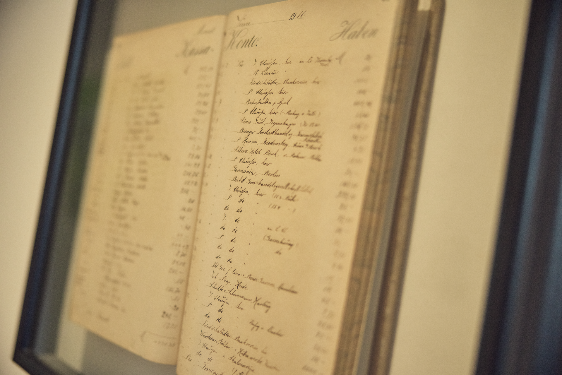 Ein geöffnetes Buch mit handschriftlichen Einträgen, die in alter deutscher Schrift verfasst sind. Die Seiten zeigen verschiedene Namen und Zahlen, möglicherweise aus einer Buchhaltungs- oder Inventarliste. Das Buch ist in einem Rahmen präsentiert.